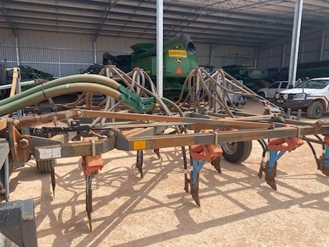 Farm sprayer with hoses and tines parked in a dusty shed beside a white pickup truck