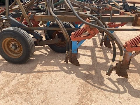 Rusty farm implement with wheels and hoses on sandy ground, viewed close-up.