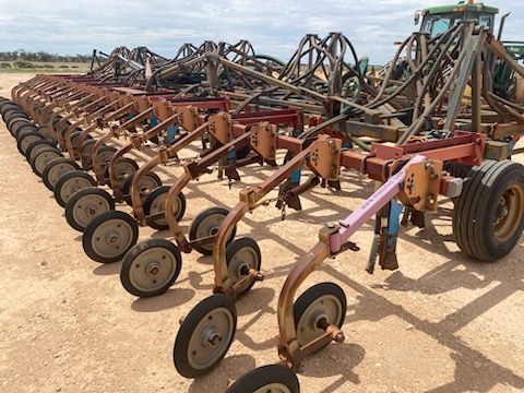 Rows of rust-colored farm implements with many wheels lined up in a dusty field