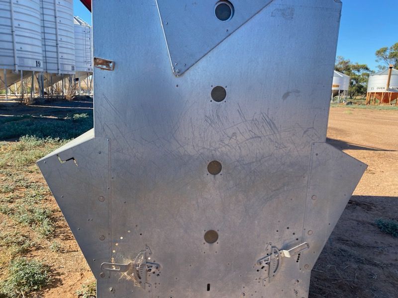 Close-up of a gray metal industrial panel with bolts and cutouts outdoors on dirt ground