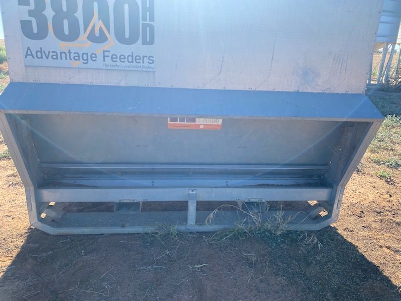 Blue Advantage Feeders livestock feeder with empty lower trough outdoors on dirt and grass.