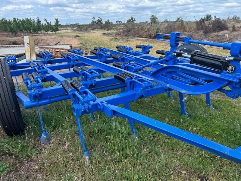 Blue agricultural implement with large black wheels sitting in a grassy field outdoors