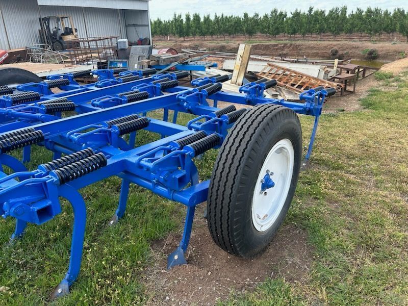 Blue agricultural implement with large wheel parked on a farm field near a shed