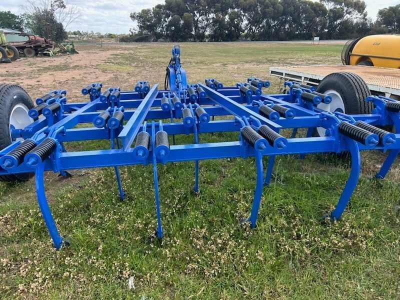 Blue agricultural tillage implement in a field, with multiple tines and wheels attached to a tractor.