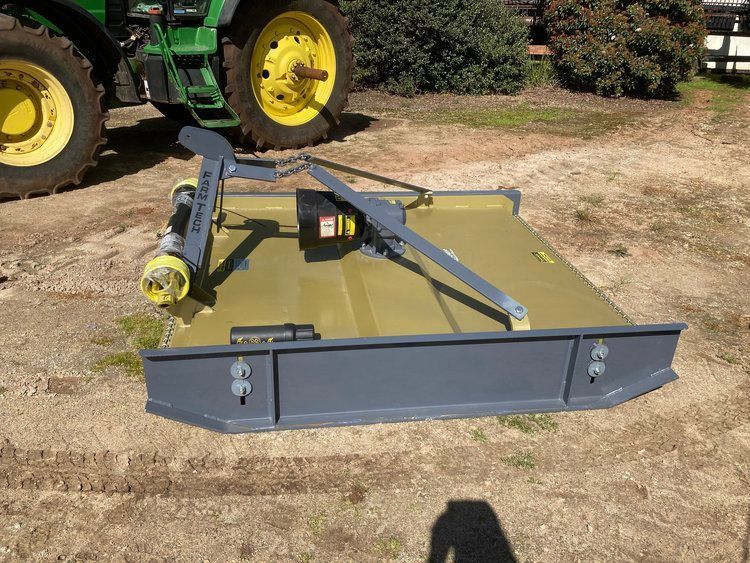 Blue tractor-mounted snow plow attachment on dry ground beside a green tractor.