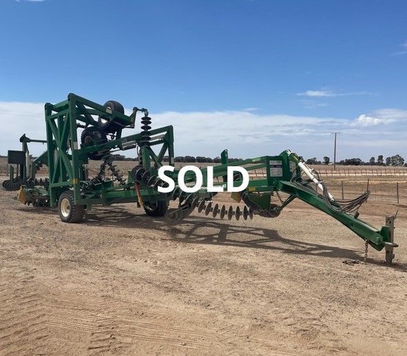 Green farm machinery on a dirt lot under blue sky, labeled “SOLD”