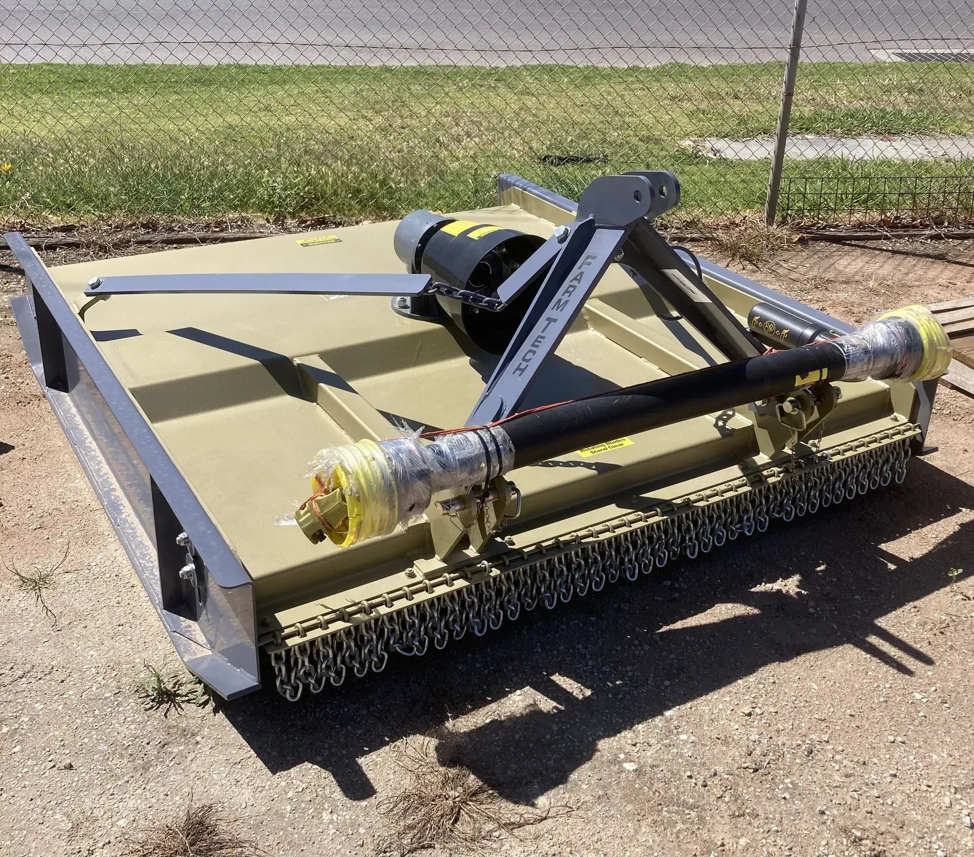 Yellow lawn mower deck attachment on pavement, with black frame and rollers in a grassy outdoor area