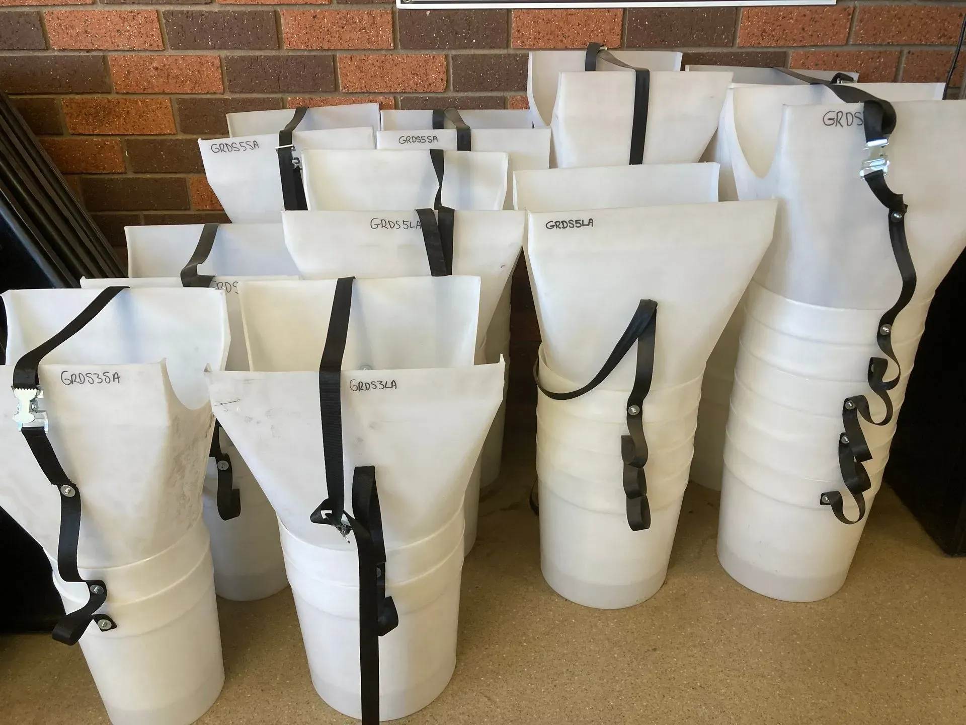 White plastic storage bins stacked in rows indoors against a brick wall.
