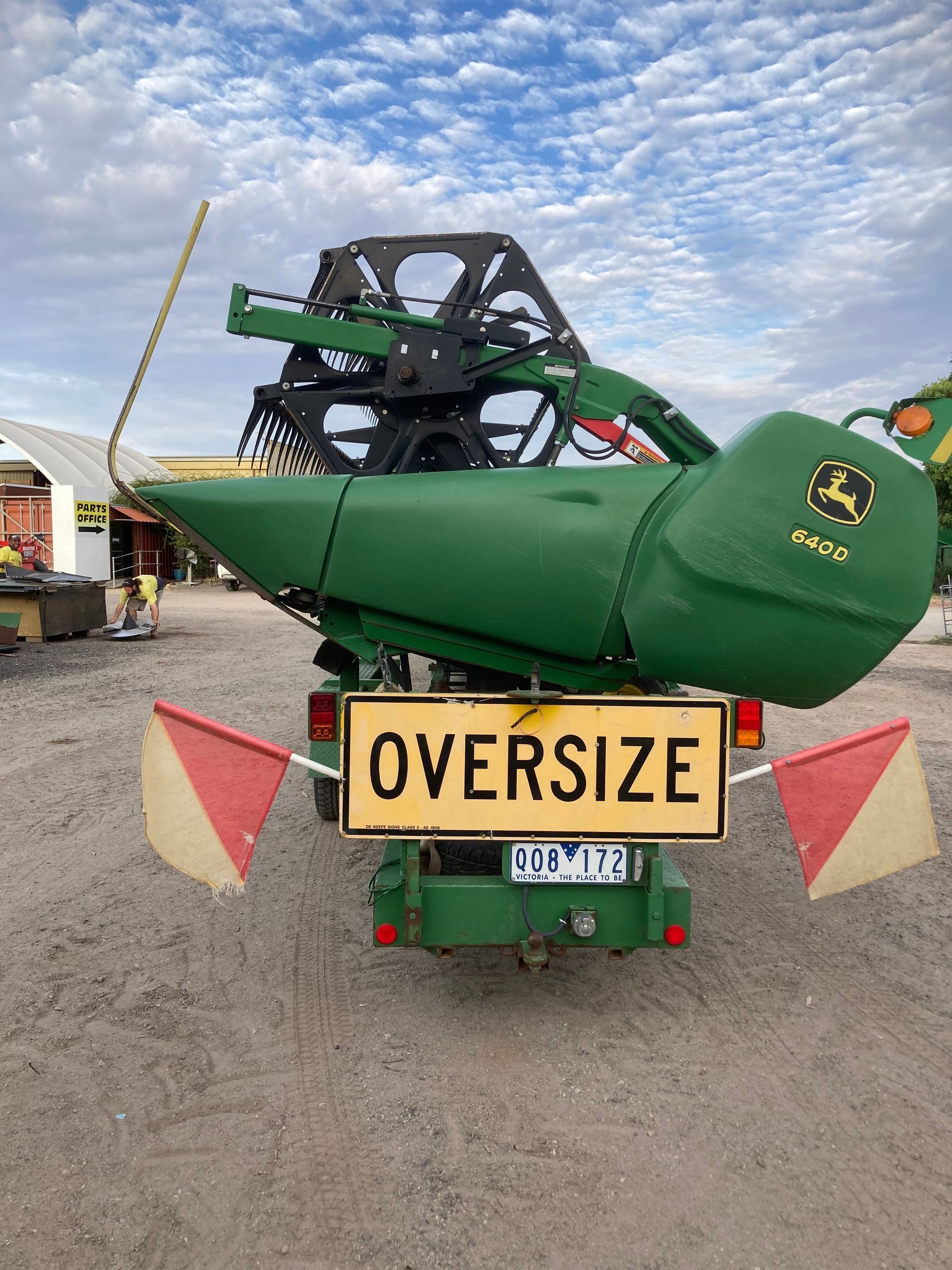 Green farm combine harvester with an OVERSIZE sign on the front, parked outdoors under a cloudy sky