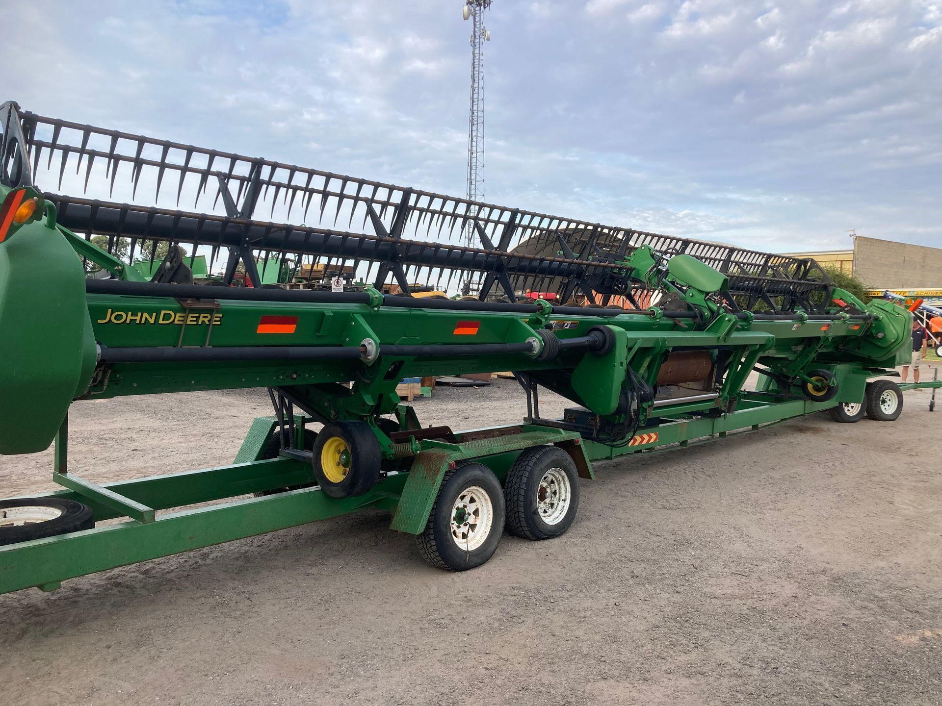 Green agricultural combine harvester on a trailer in an outdoor lot under a cloudy sky