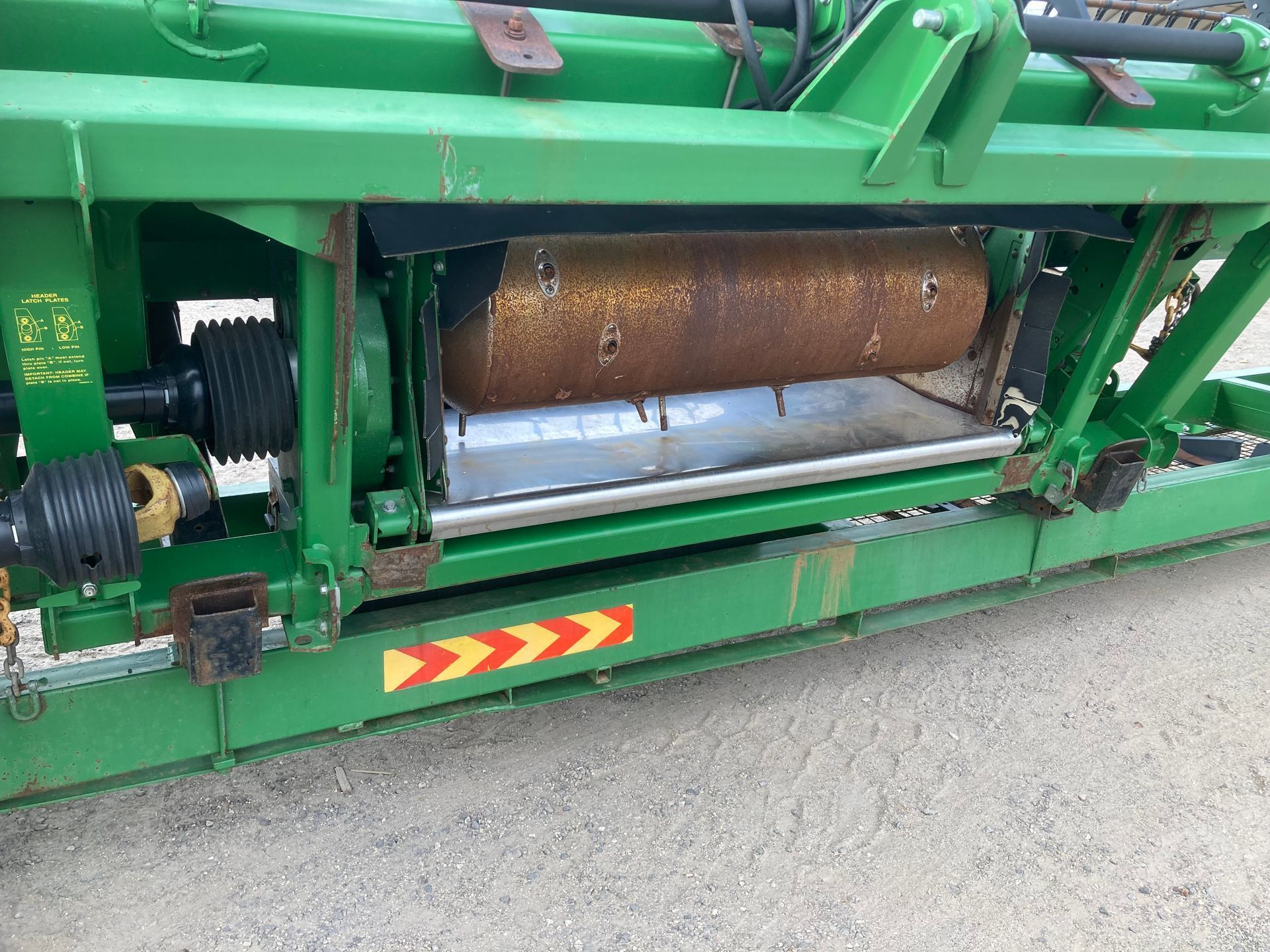 Close-up of green farm machinery with rusted metal drum and black rollers on a paved surface