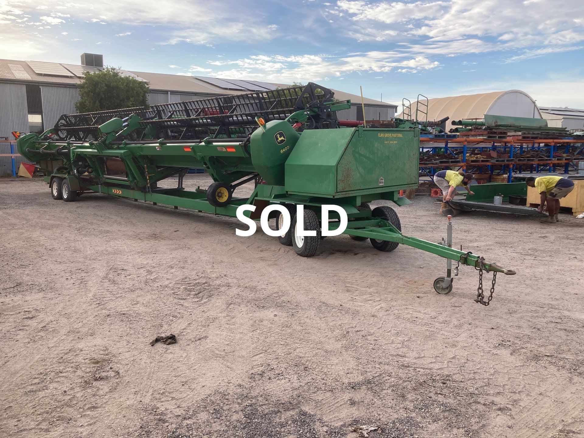 Green farm implement trailer in an outdoor lot, marked “SOLD” at a machinery auction