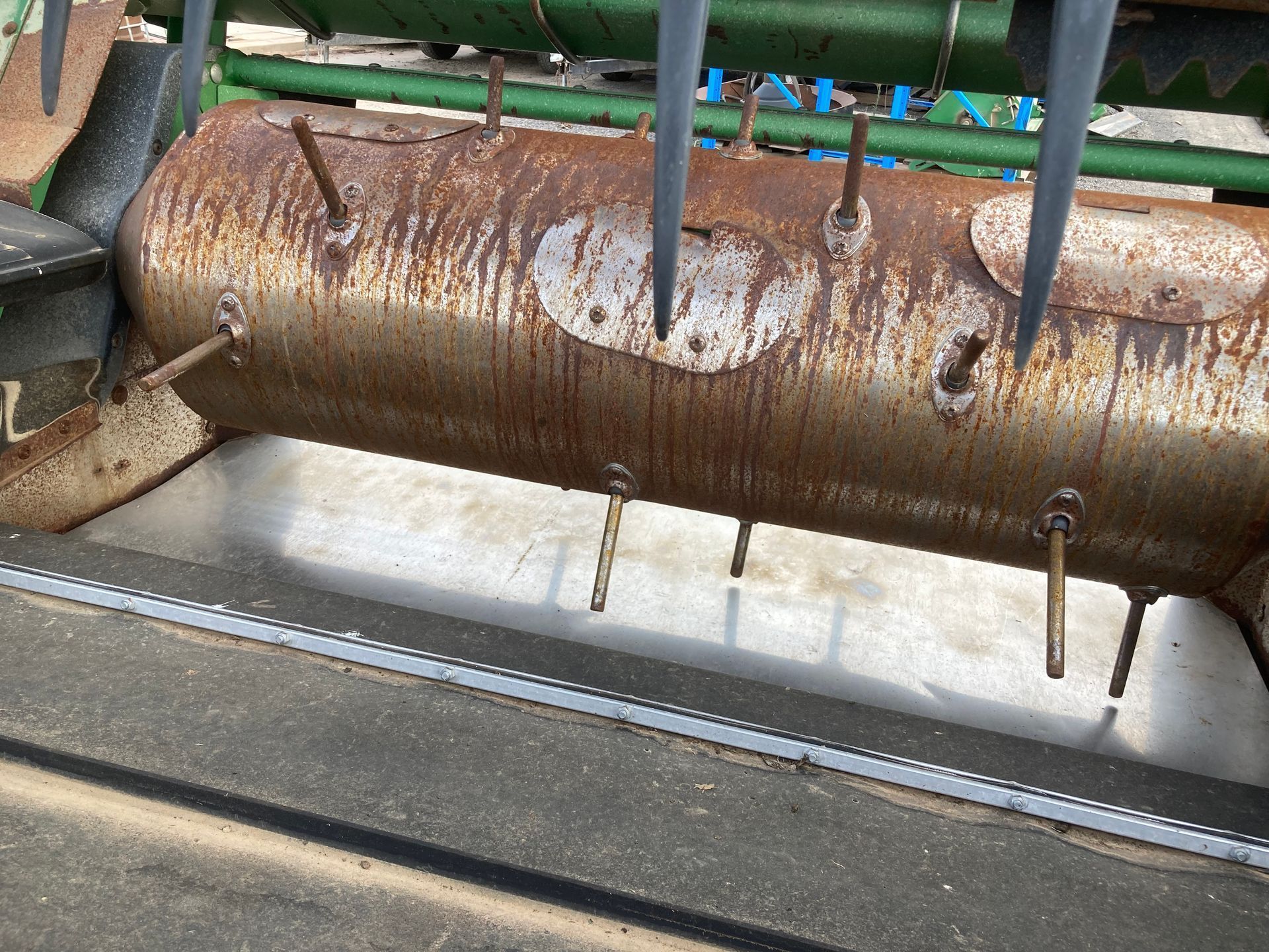 Rusty metal cylinder with bolts and hanging rods over a concrete channel