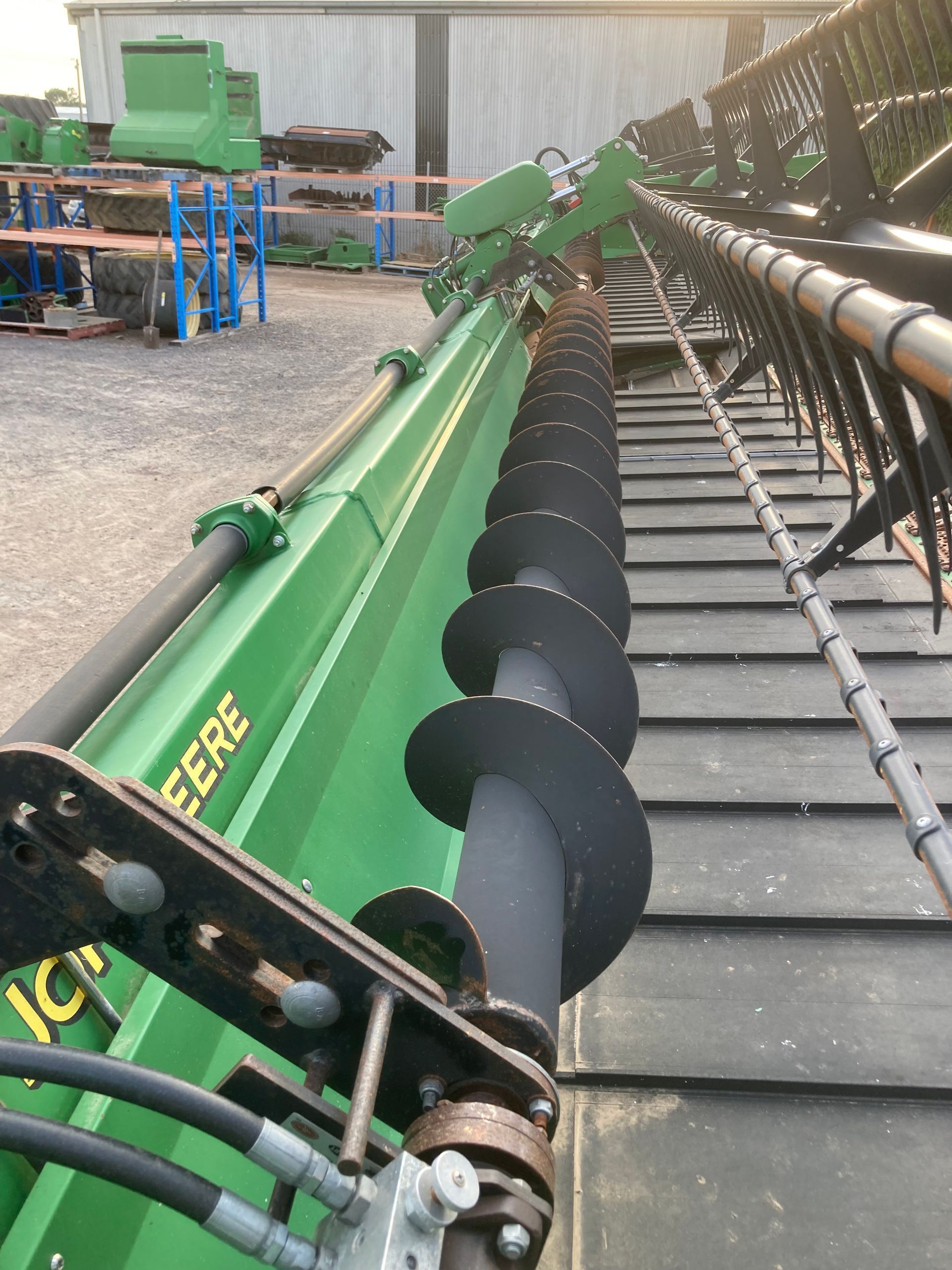 Green agricultural combine header with black cutting reel in a warehouse