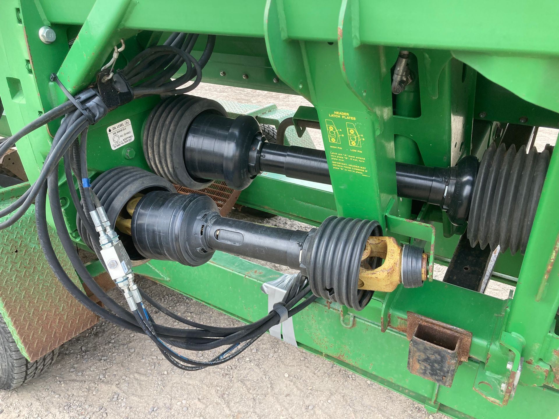 Close-up of green farm machinery with exposed drive shafts and pulleys under a metal frame