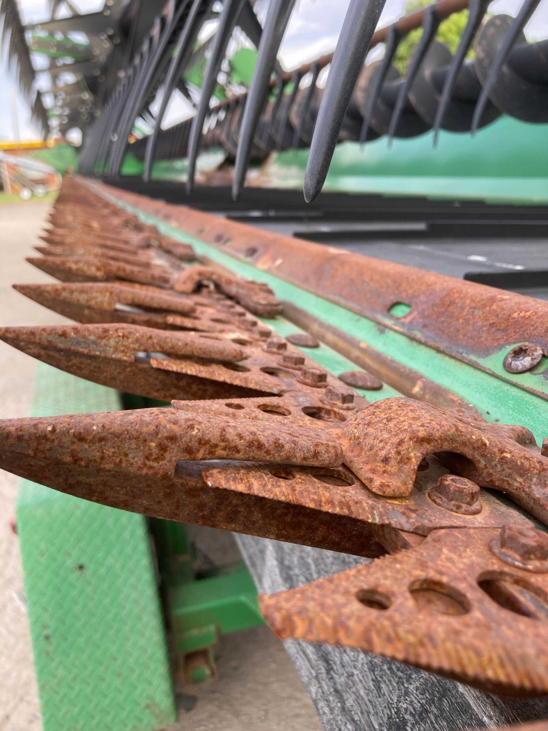 Close-up of rusted metal teeth on a green agricultural machine outdoors