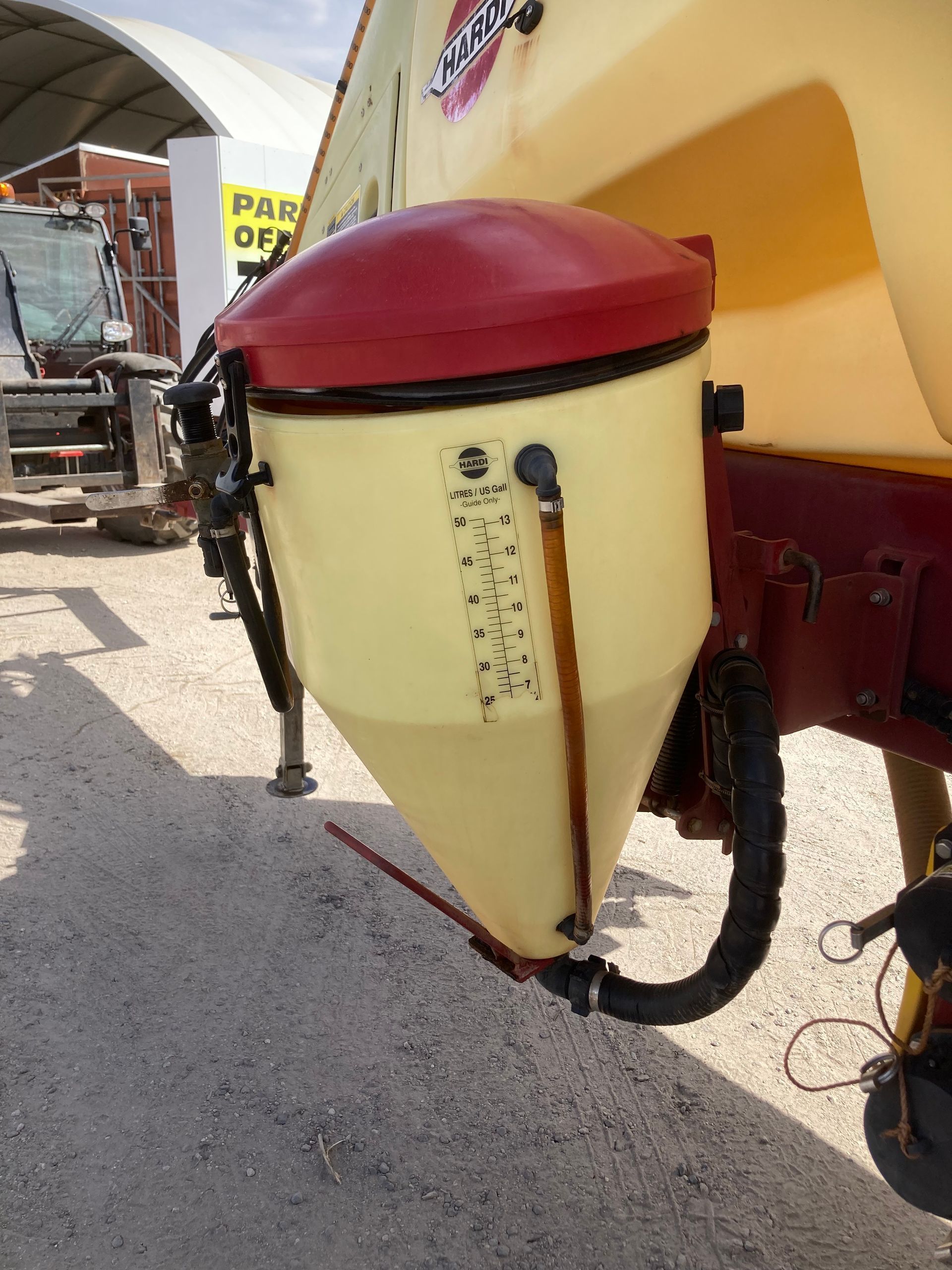 Red-and-cream agricultural machine hopper with hose and wheel mounted on a trailer outdoors
