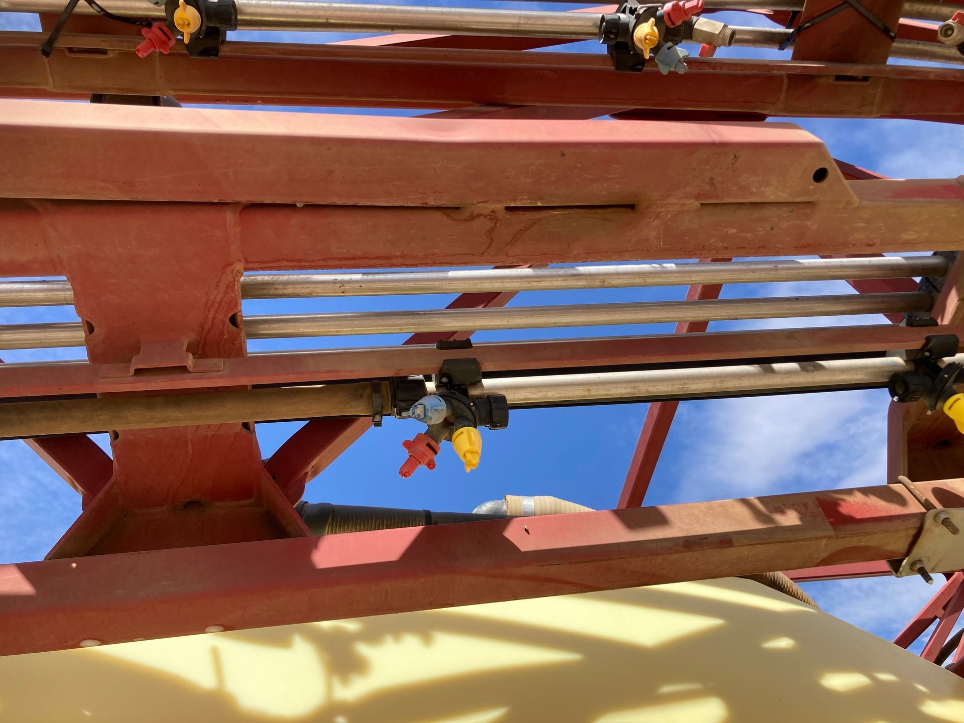 Close-up of a rust-red metal structure with slats and hanging cables against a bright sky