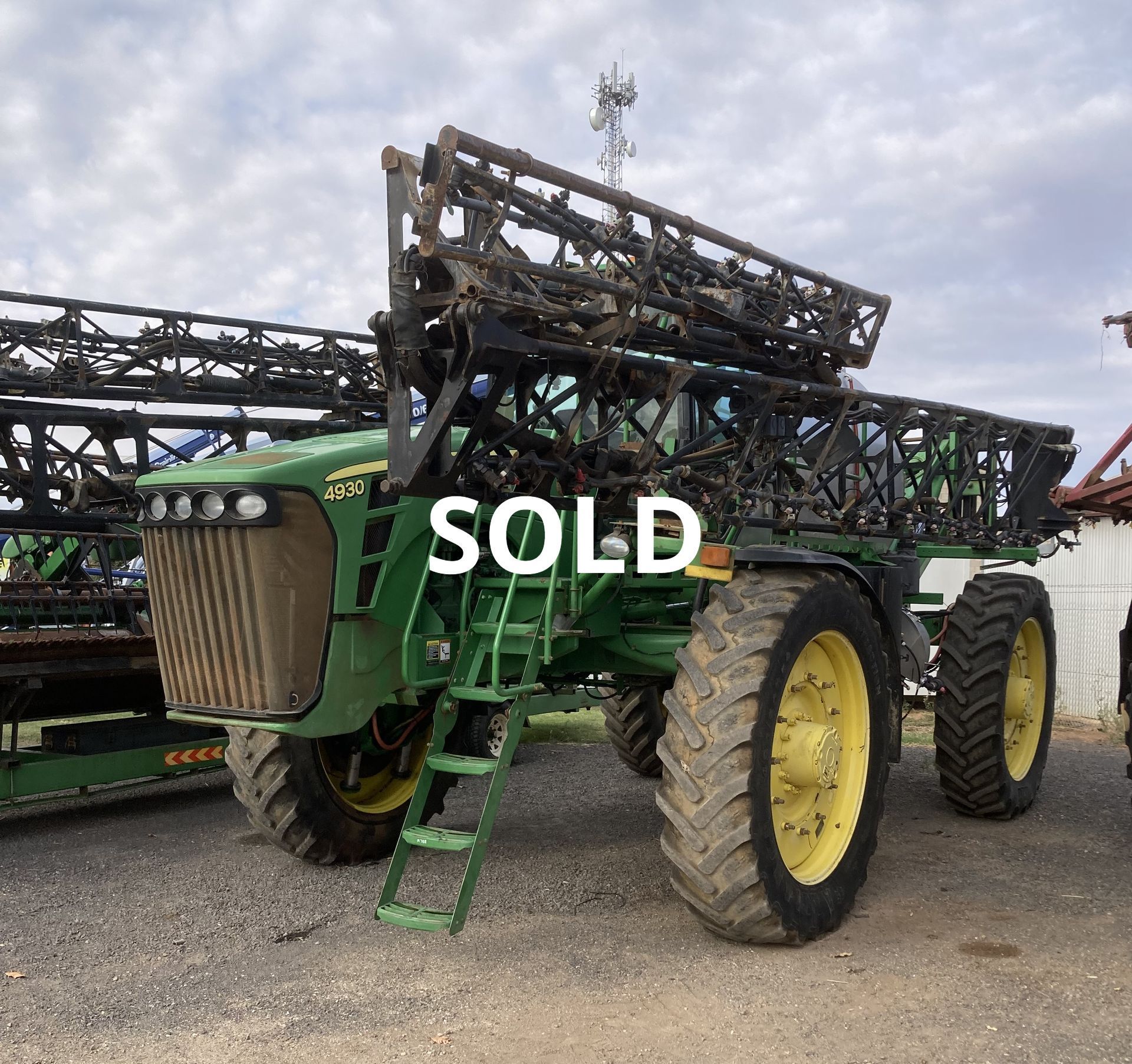 Green agricultural sprayer on a lot with “SOLD” text overlay, under a cloudy sky