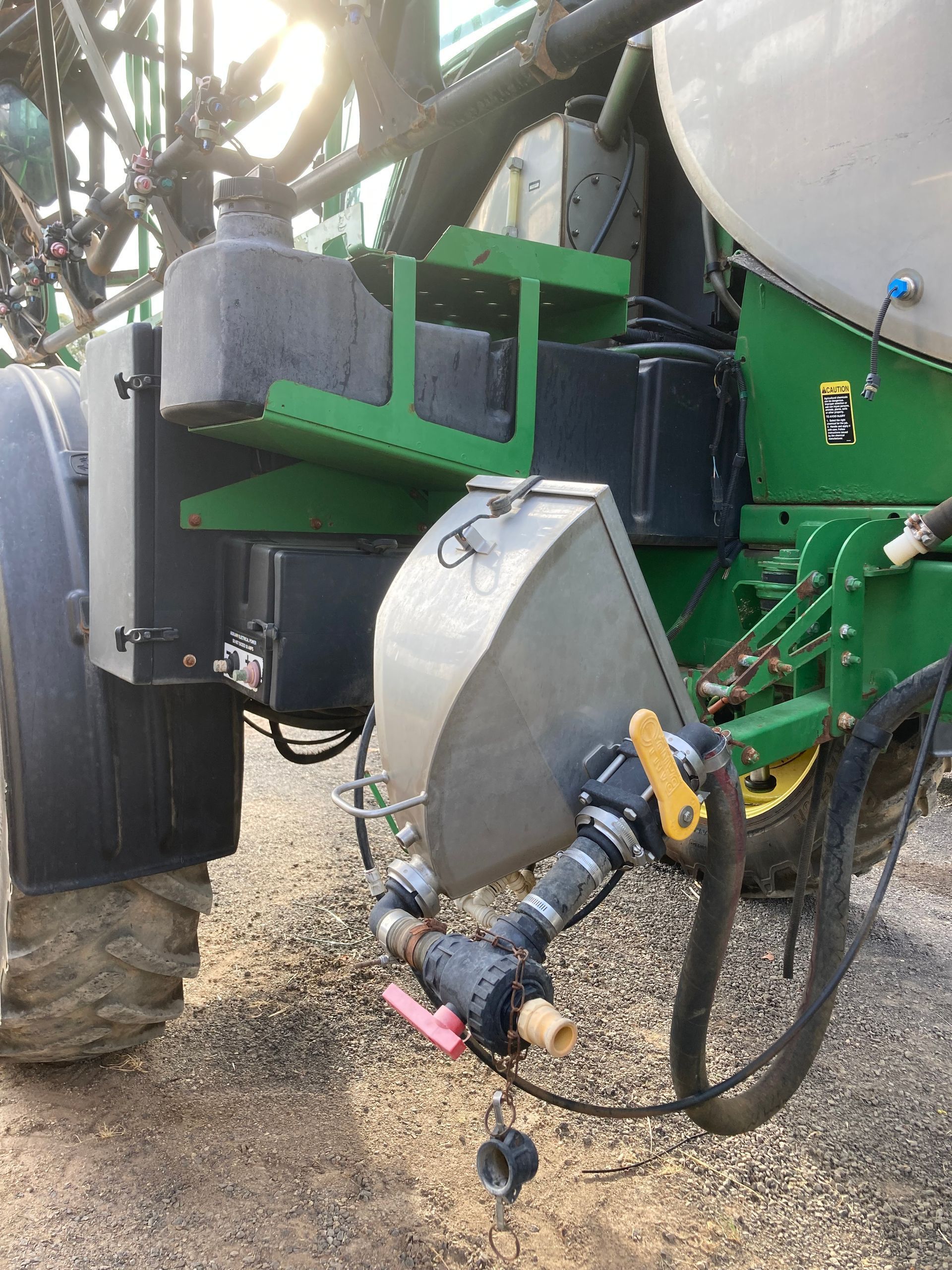 Close-up of green agricultural machinery with hoses, metal parts, and a muddy tire in a farm field