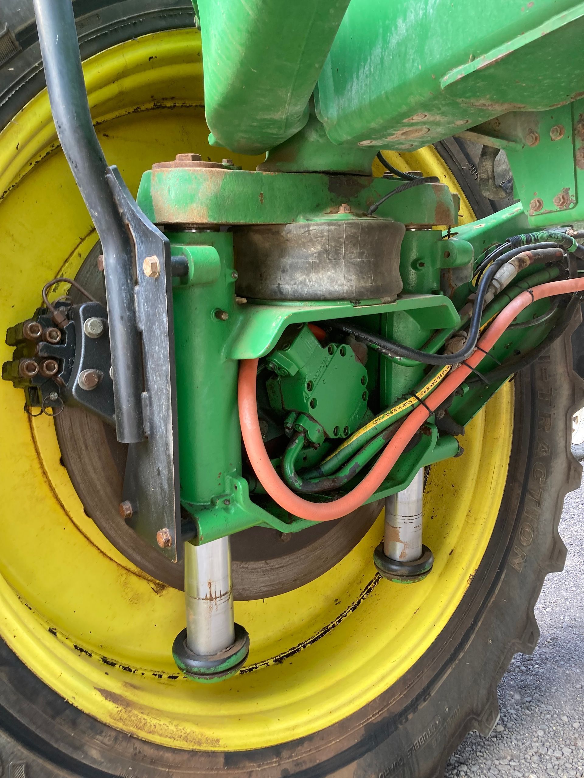 Close-up of a yellow wheel and green farm machinery with hoses and metal parts.