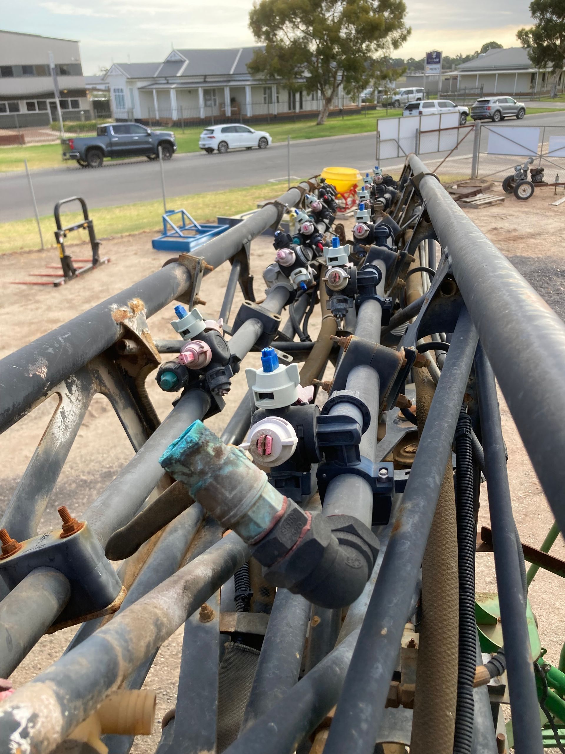 Pipes and valves stacked on a trailer at a roadside worksite, with houses and parked cars in the background