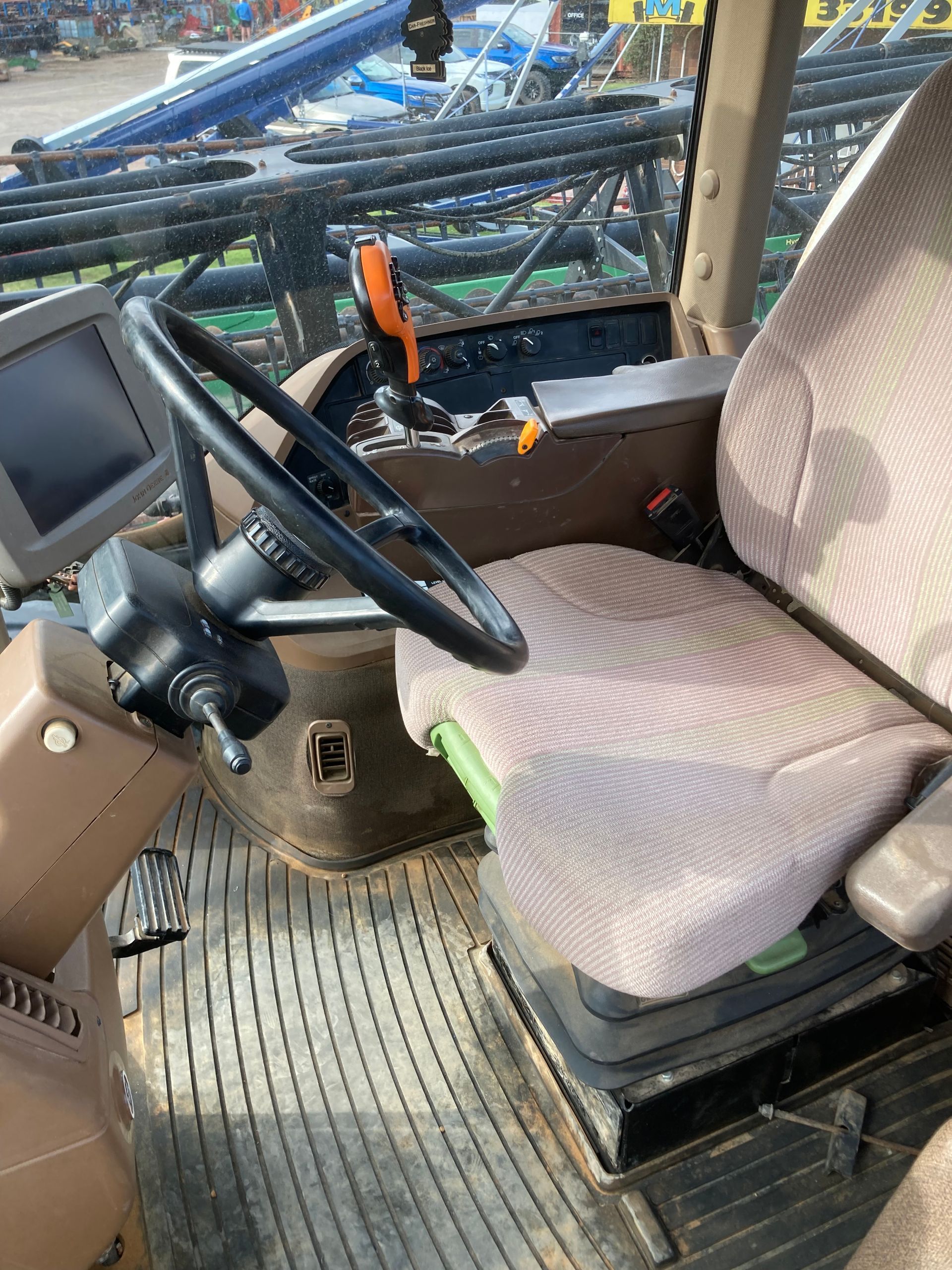 Operator seat and steering controls inside a construction vehicle cab, with a monitor and control levers.