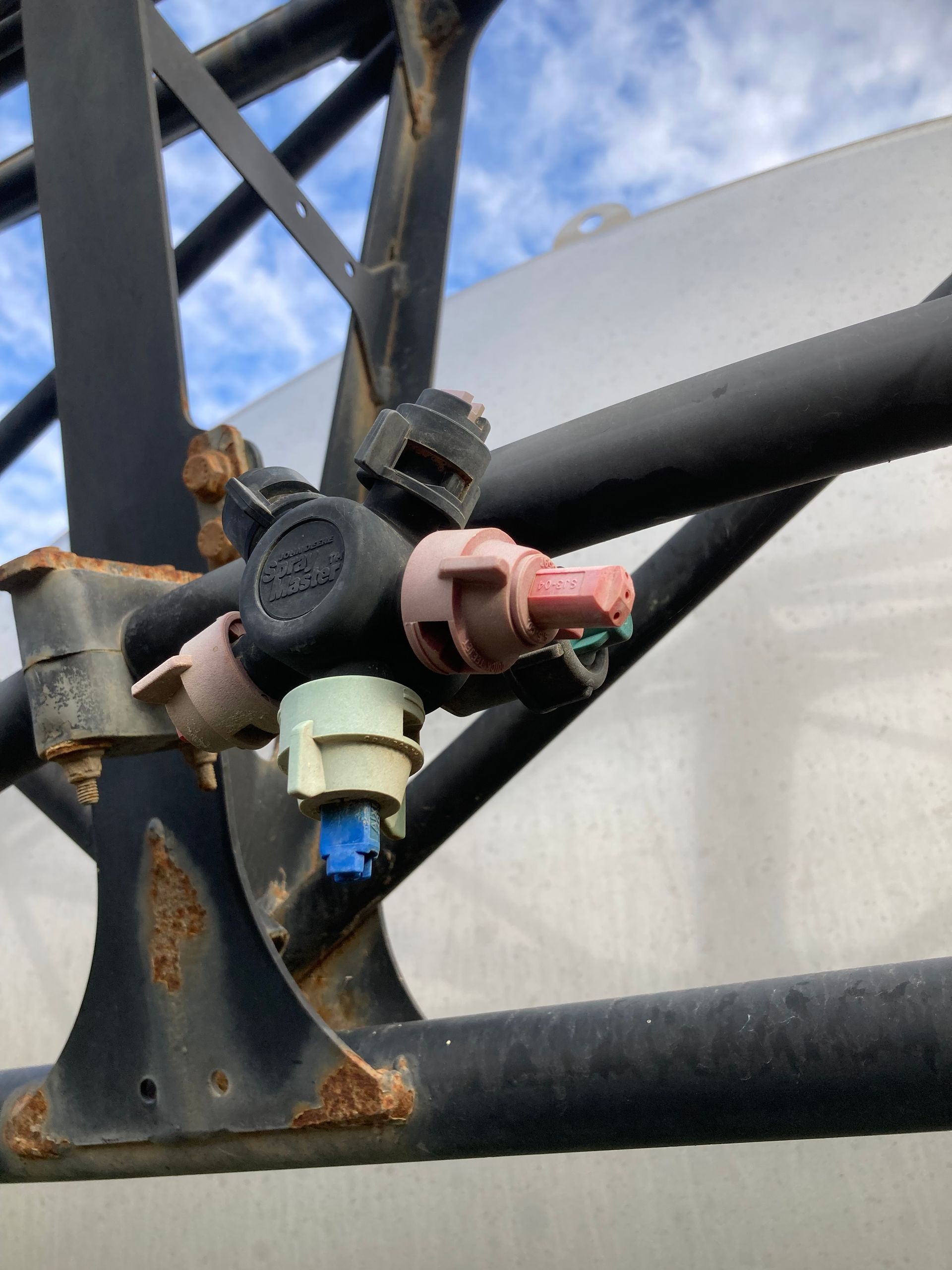 Close-up of industrial pipes with valves and fittings against a metal tower and sky