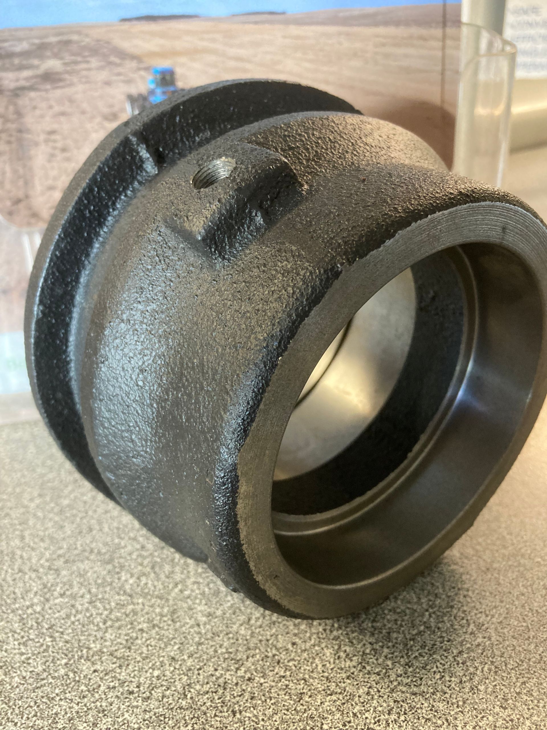 Black textured plastic pipe fitting with a wide opening, resting on a countertop against a blurred background