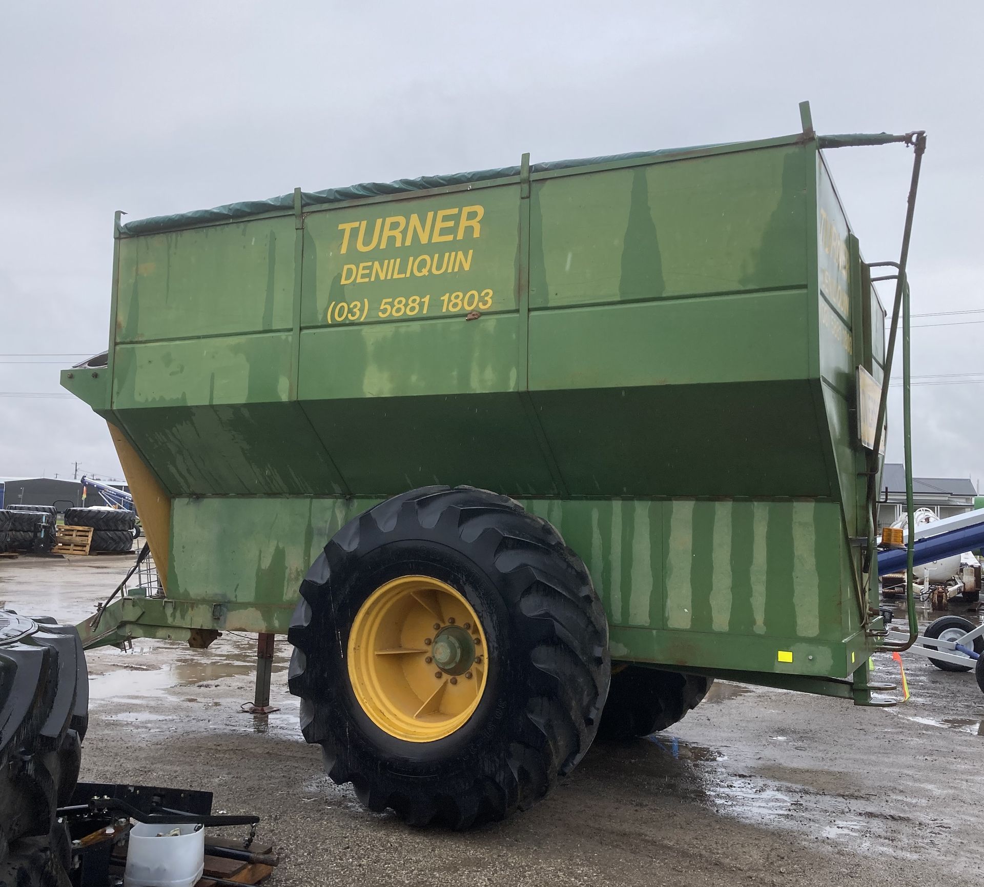 Green TURNER dump trailer with large black wheel parked on a wet gravel lot