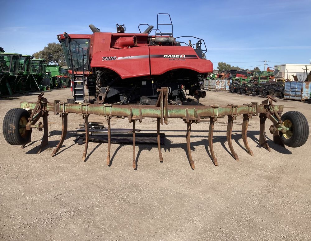 Red agricultural combine harvester with a wide tillage attachment parked on a gravel lot