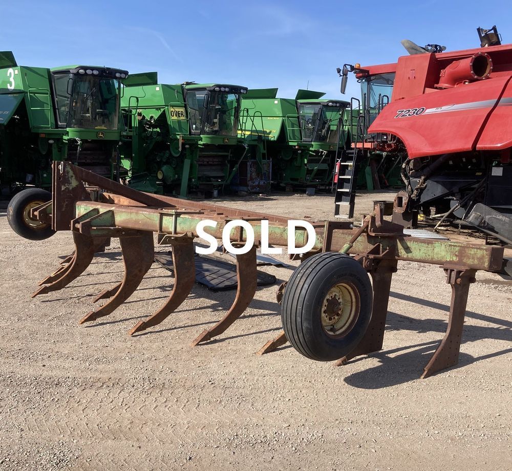 Farm equipment lot with a rusted plow in front of green machinery, marked SOLD.