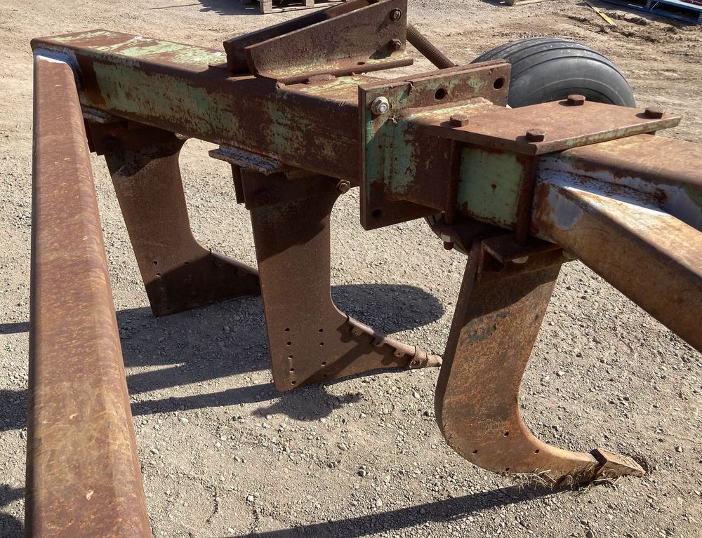Rusty farm implement with metal tines and a wheel on gravel ground