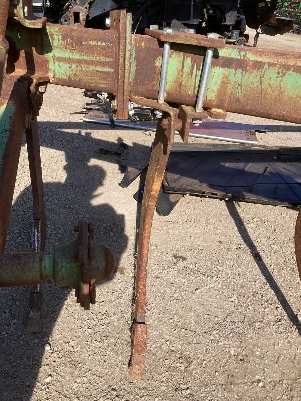 Rusty green metal farm implement on a gravel surface, with a long support leg and attached wheel.