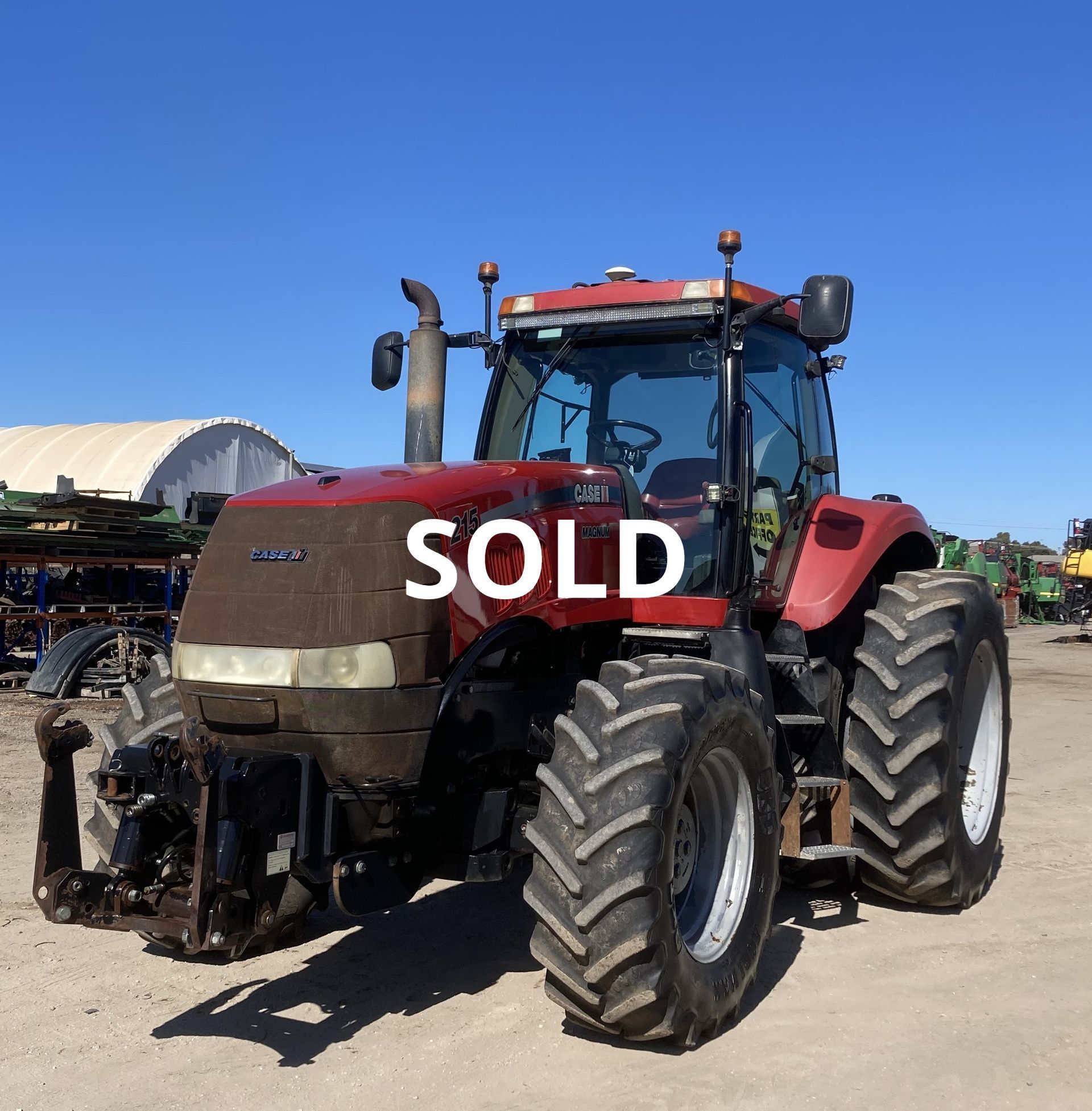Red tractor parked outdoors with a large white “SOLD” sign on the front.