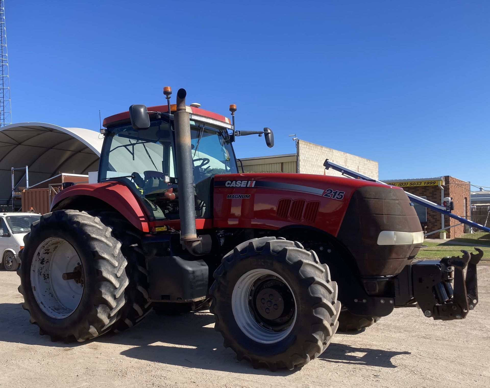 Red tractor parked outdoors on a sunny day, with large tires and farm equipment attached.