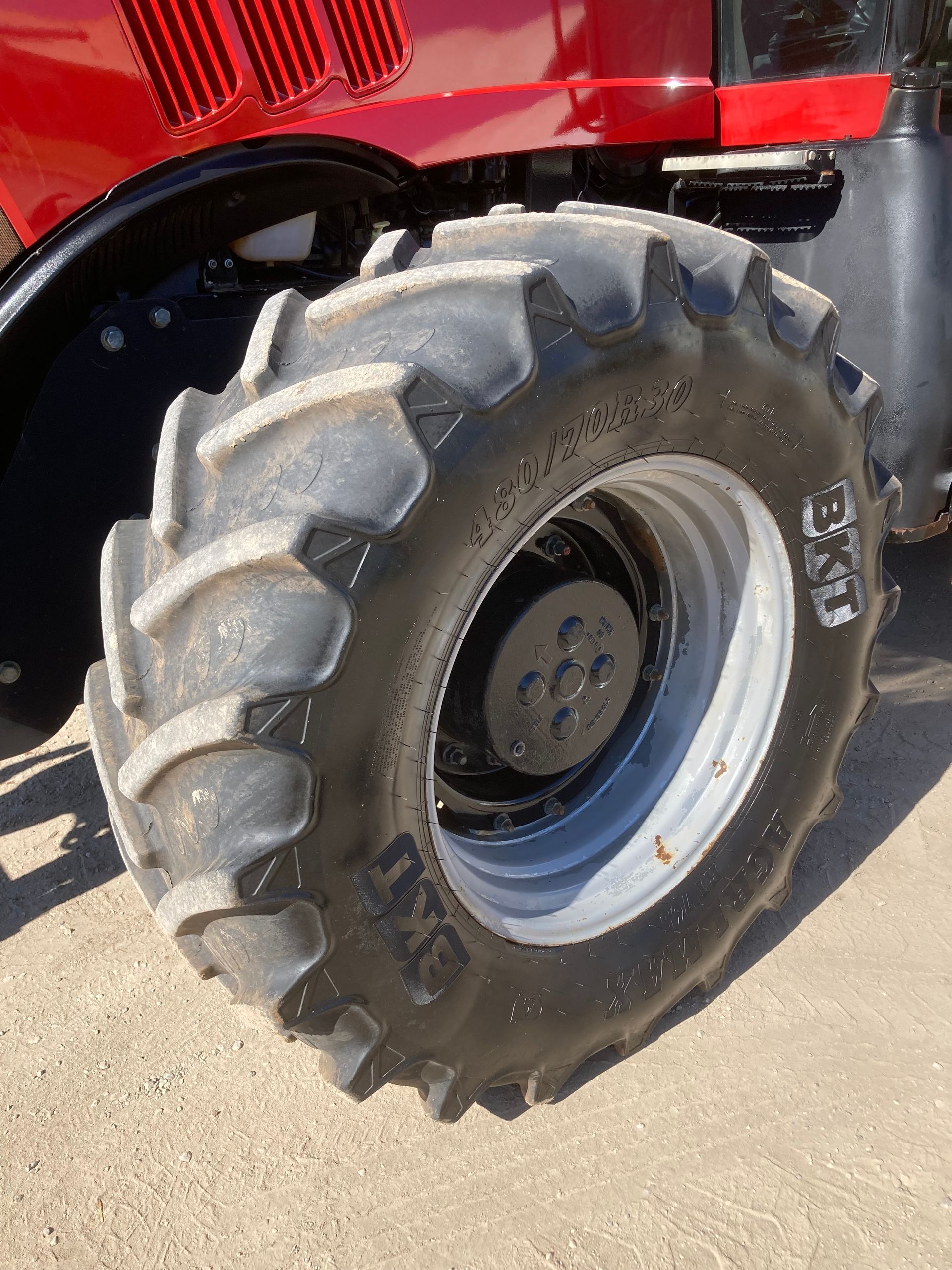 Close-up of a red tractor wheel with a large muddy tire on pavement