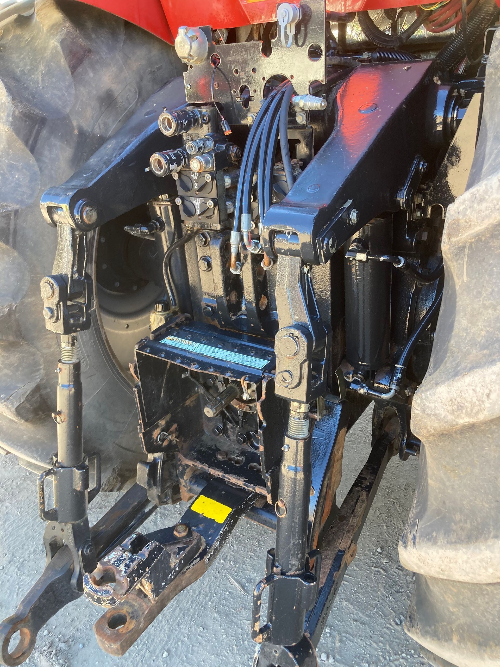Black hydraulic tractor attachment with hoses and metal frame on a workshop floor