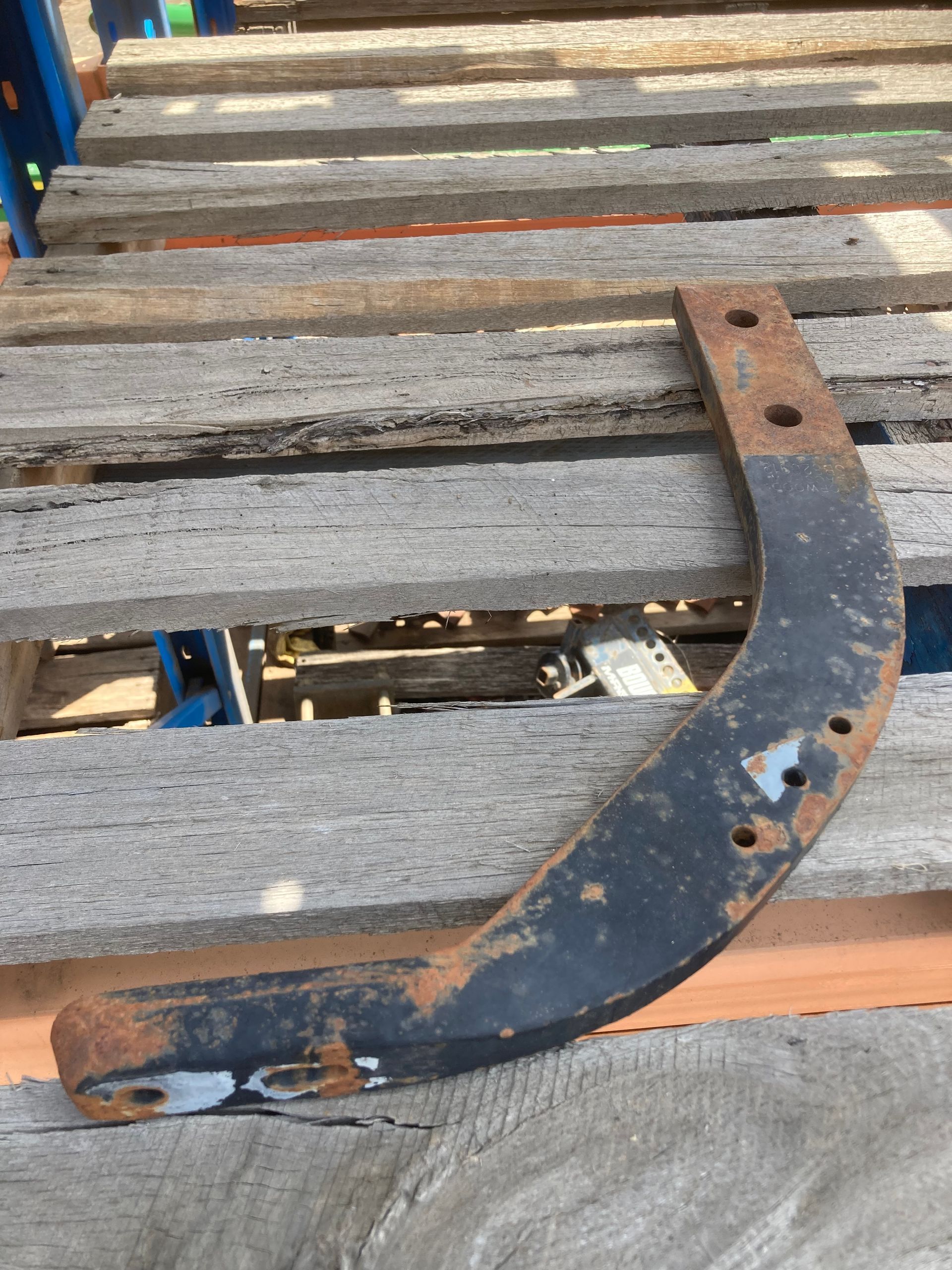 Rusty curved metal bracket resting on weathered wooden slats outdoors