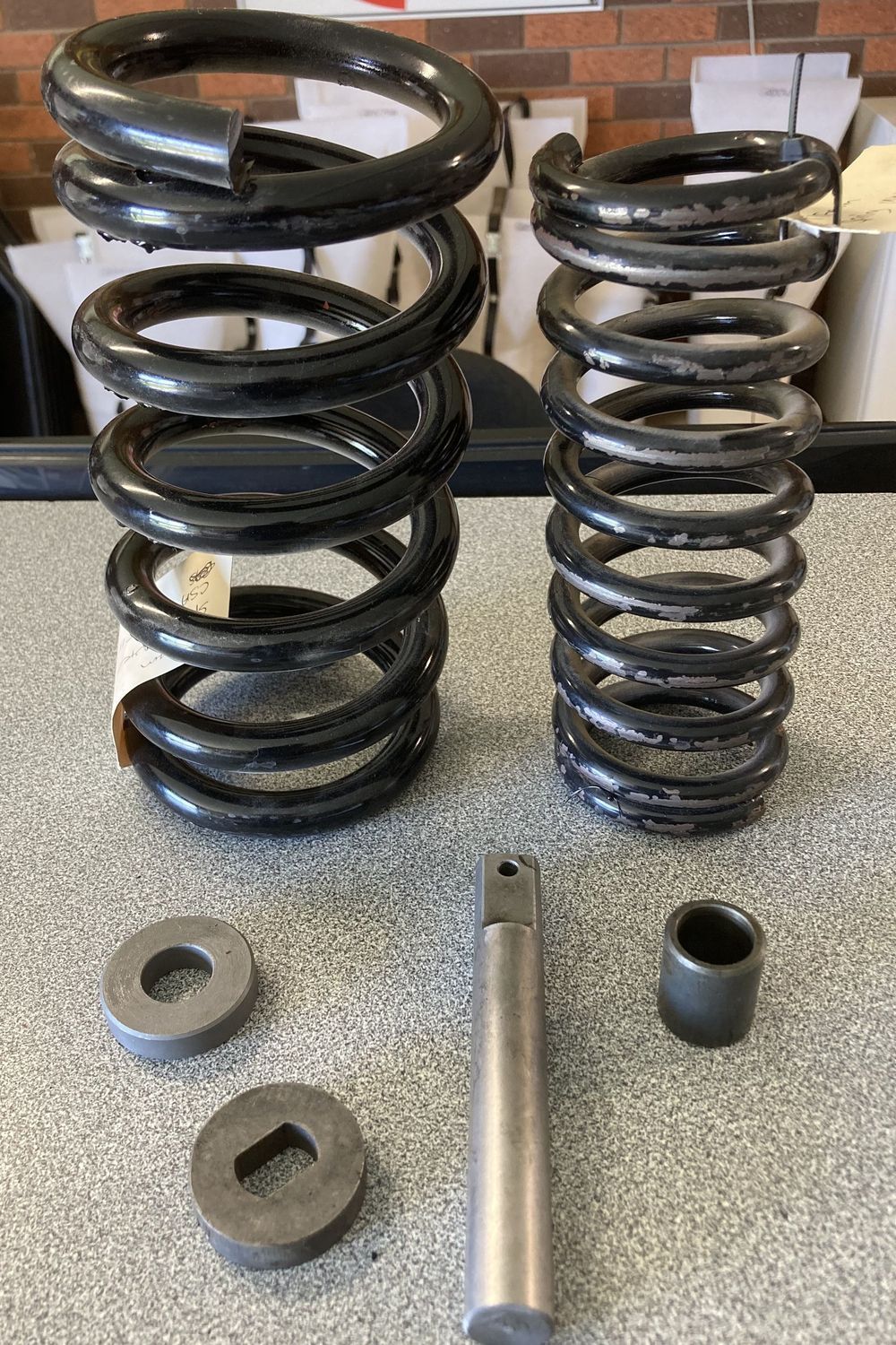Two black coil springs, metal tubes, and two square washers arranged on a tabletop.