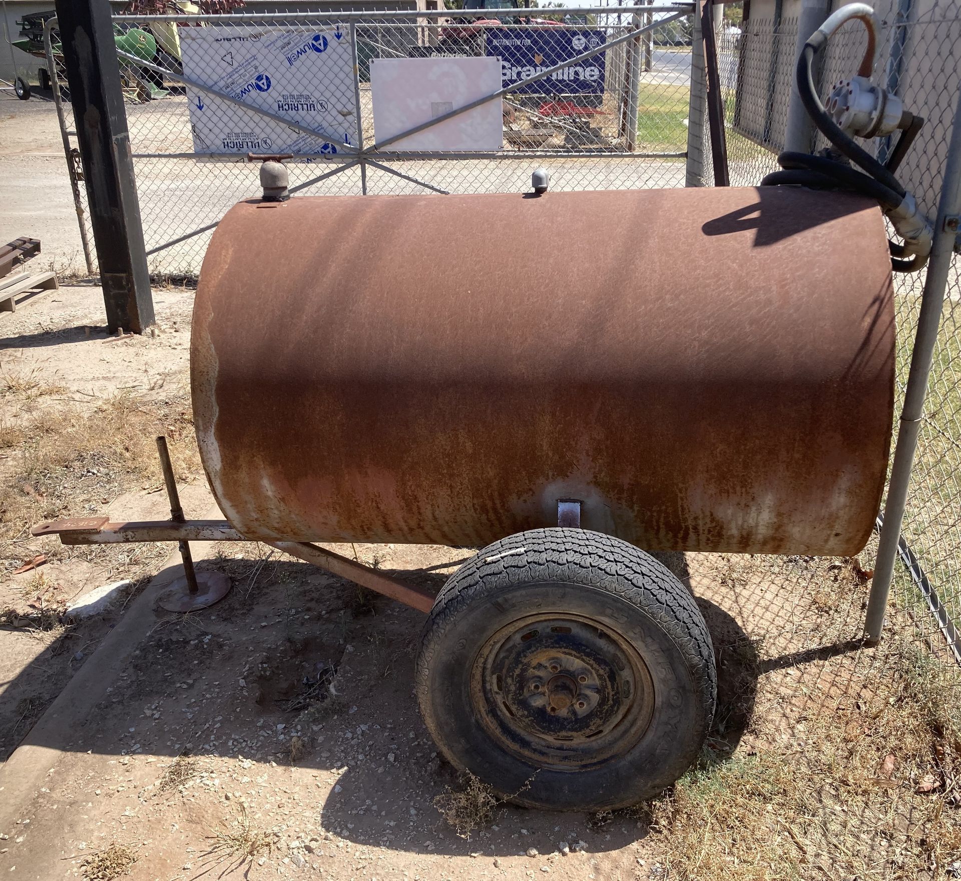 Rusty cylindrical metal trailer on two wheels in a dry outdoor yard.