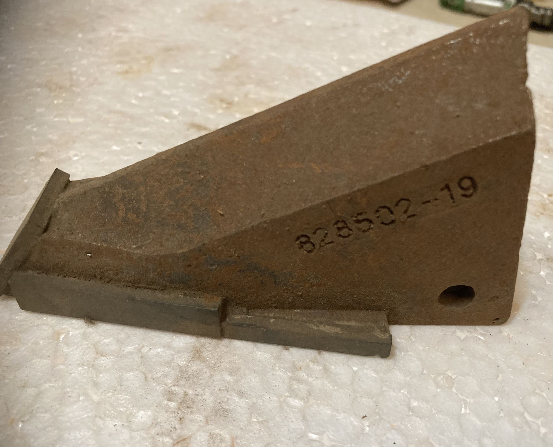 Rusty metal wedge part with stamped number 823582-19 on a foam surface