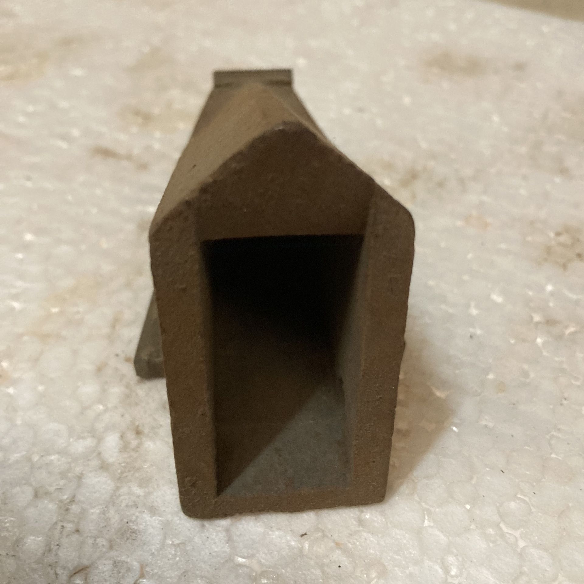 Brown hollow rectangular metal tube end on a light textured surface