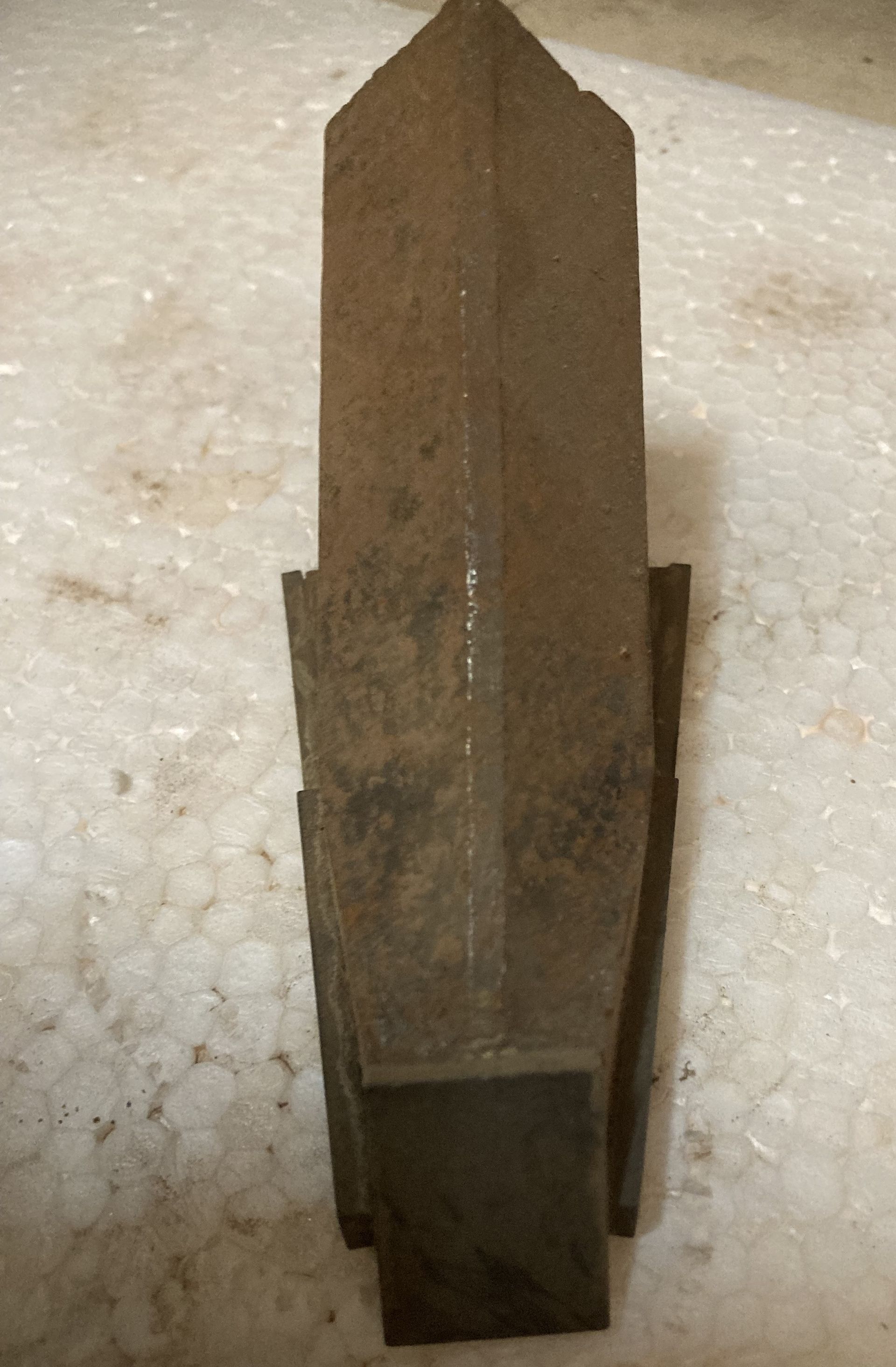 Rusty metal wedge-shaped tool standing upright on a white textured surface