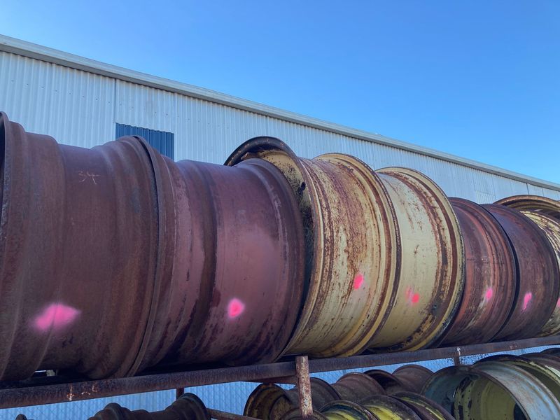Rusty industrial pipes lined up outdoors against a blue sky and a metal building.