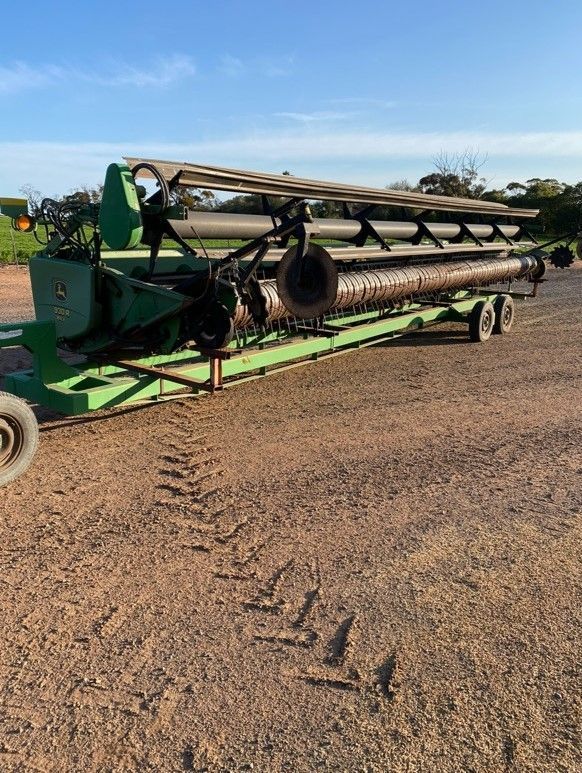 Green combine harvester header on a gravel road under a blue sky