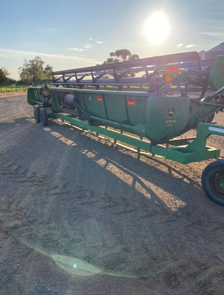 Green agricultural combine harvester parked on a gravel road at sunset with bright sun glare.