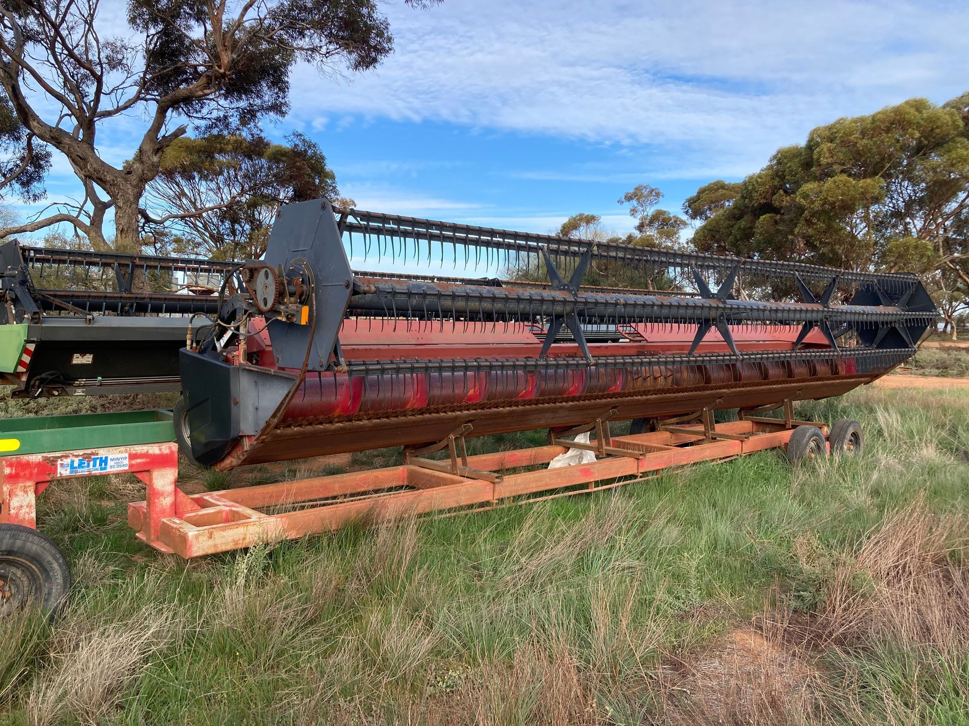 Large red agricultural machine on a wooden pallet in a grassy field under a blue sky.