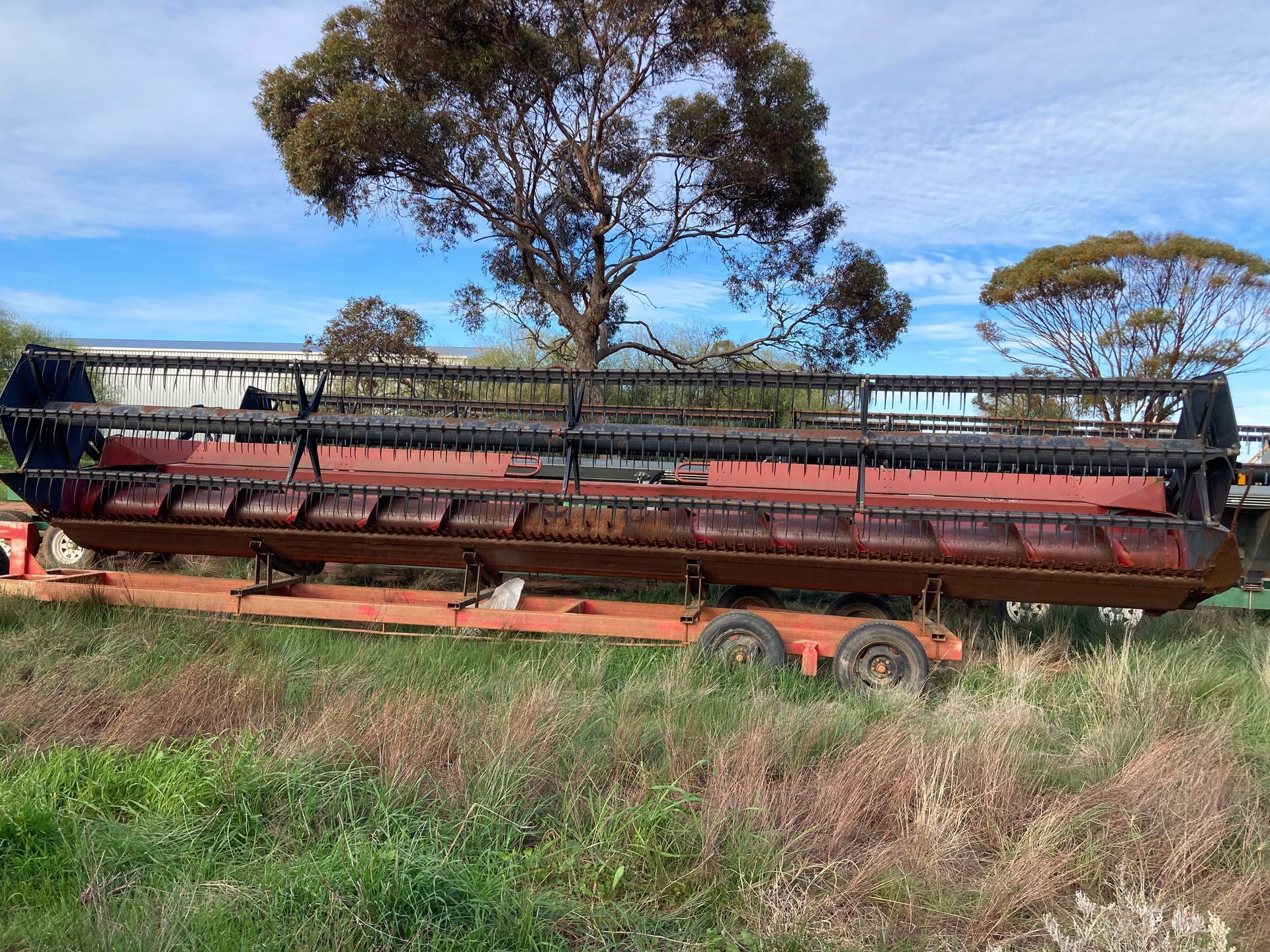 Old rusty red farm harvester trailer in tall grass with trees in the background