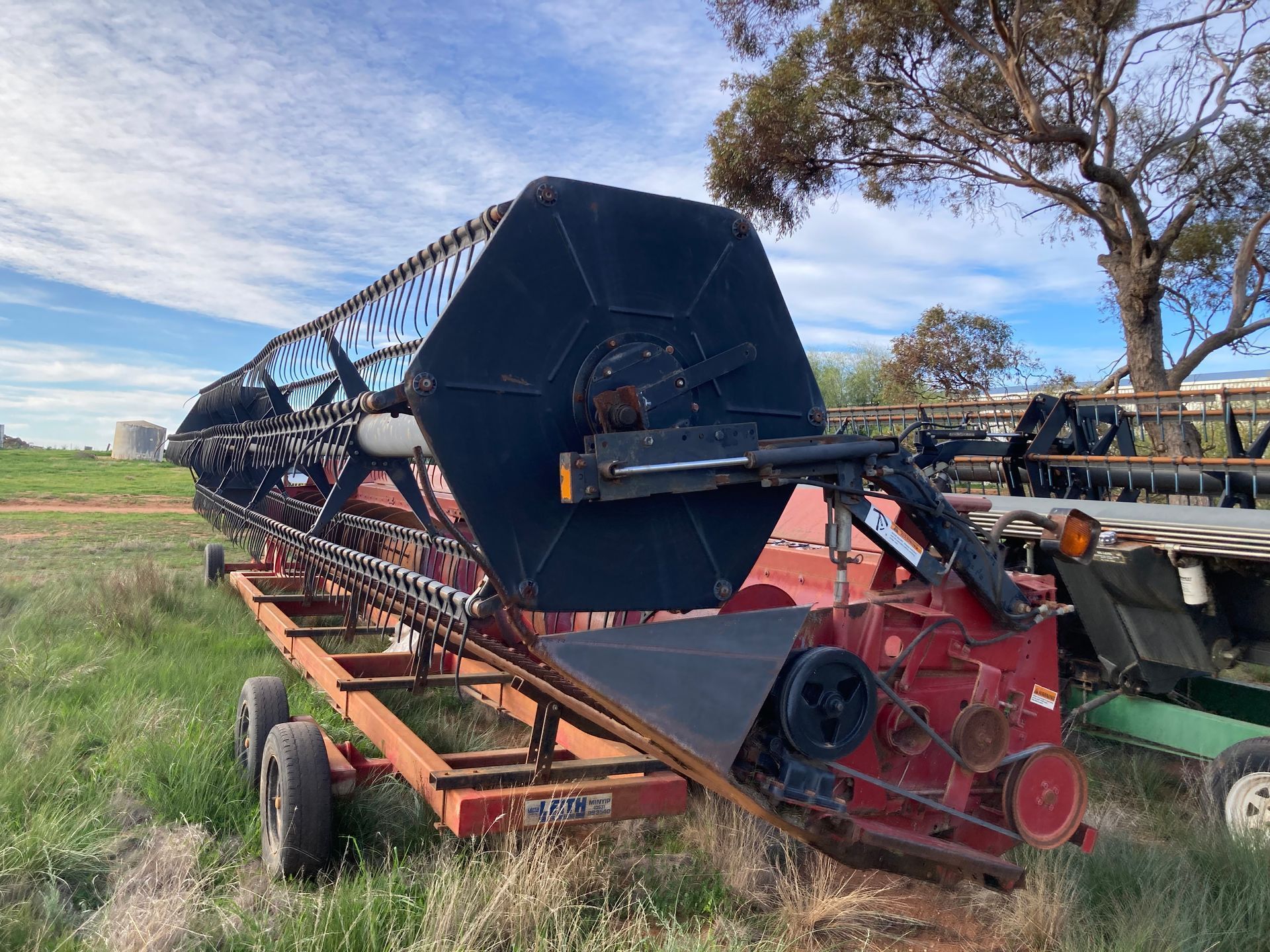 Large black and red farm combine harvester parked in a field under a blue sky